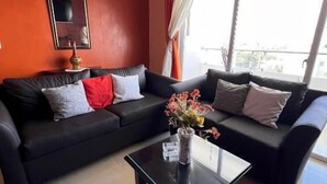 A living room with a black sofa set, a glass coffee table, and a vase with flowers. - Bello Apartamento en Santiago con Todas las Comodidades (Santiago de los Caballeros)