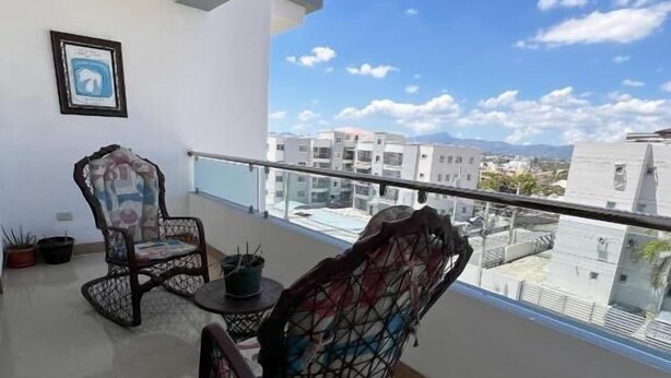 A balcony with two wicker chairs, a small table, and potted plants. - Bello Apartamento en Santiago con Todas las Comodidades (Santiago de los Caballeros)