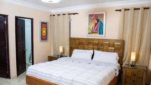 A bedroom with a wooden bed, two bedside tables with lamps, a framed picture on the wall, and a door to the left. - Casa Linda Beautiful Villa (Sosúa)