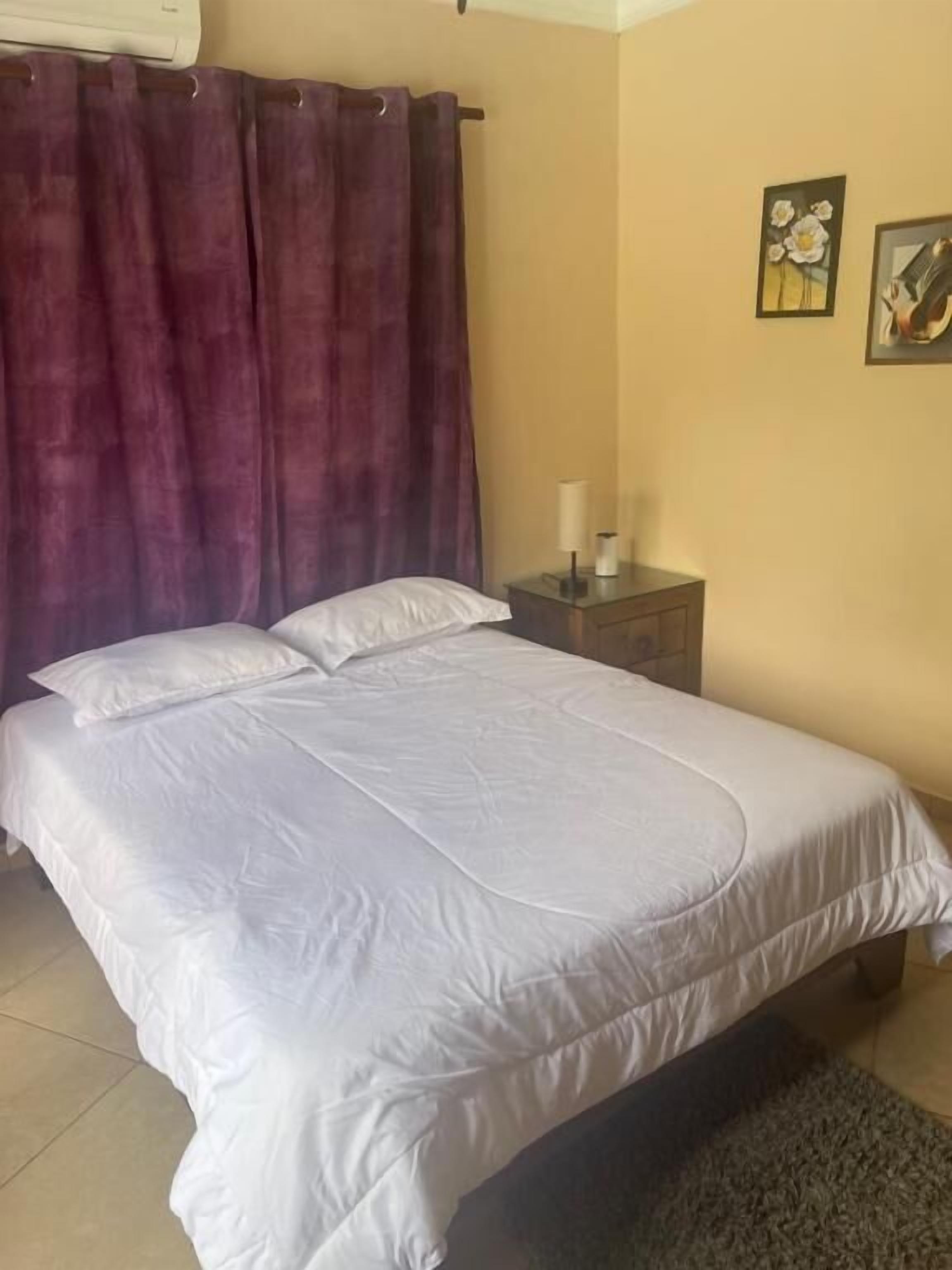 Un dormitorio con cama, mesita de noche, lámpara y dos cuadros.