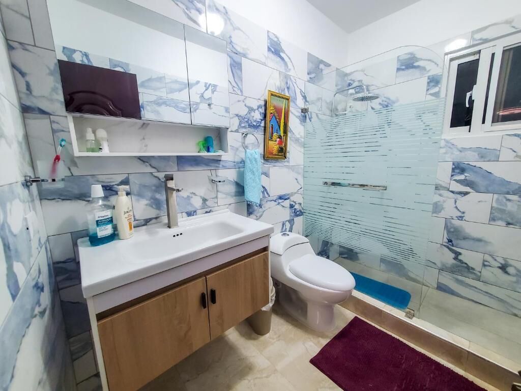 A bathroom with a marble backsplash, a white sink, a toilet, and a glass shower enclosure.
