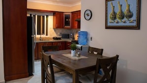 A dining area with a wooden table and chairs, a water dispenser, and a clock on the wall. - Casa Linda Beautiful Villa (Sosúa)