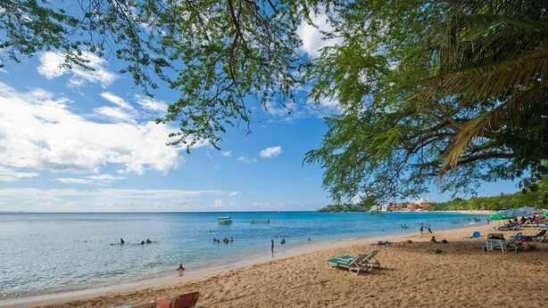A beach with clear blue water, people swimming and sunbathing, and a few boats in the distance. - Luxury in the Caribbean (Sosúa)