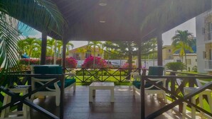 A covered outdoor seating area with white chairs and tables, surrounded by lush greenery and palm trees. - Luxury in the Caribbean (Sosúa)