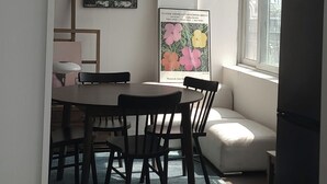 Ein Essbereich mit rundem Tisch und Stühlen, einer Uhr an der Wand und einem Blumenplakat.