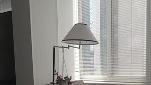 Ein Schlafzimmer mit einem Bett, einem Sessel, einer Stehlampe und einem Fenster mit Jalousien.