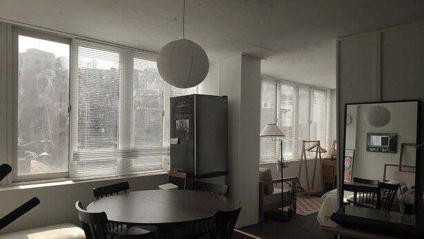 Eine moderne Küche mit einem runden Esstisch, Stühlen, einem Kühlschrank und einem großen Fenster mit Jalousien.
