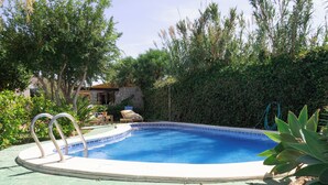 En pool med stendæk, omgivet af grøn vegetation og en støttemur.