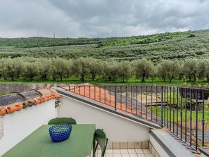 Eine Terrasse mit Tisch und Stühlen, mit Blick auf eine Olivenhain und eine hügelige Landschaft.