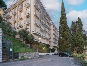 Ein mehrstöckiges Wohngebäude mit Balkonen, einer Steinmauer und einem Parkplatz mit Autos.
