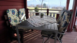 A covered outdoor seating area with a table and chairs, a vase with flowers, and a view of a mountain landscape. - Holiday Home LiRa (Villach)