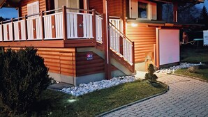 A two-story wooden house with a balcony, a small front porch, and a paved driveway. - Holiday Home LiRa (Villach)