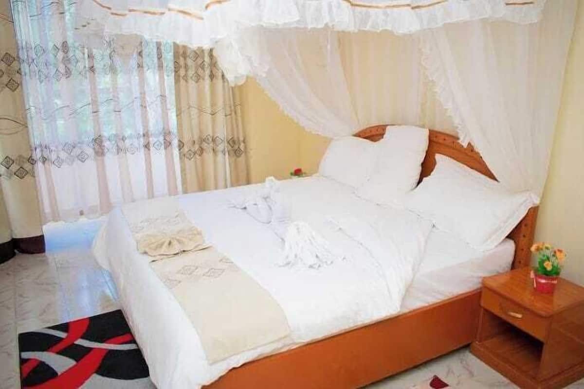 Una cama con dosel, una mesita de noche con un florero y una alfombra estampada.