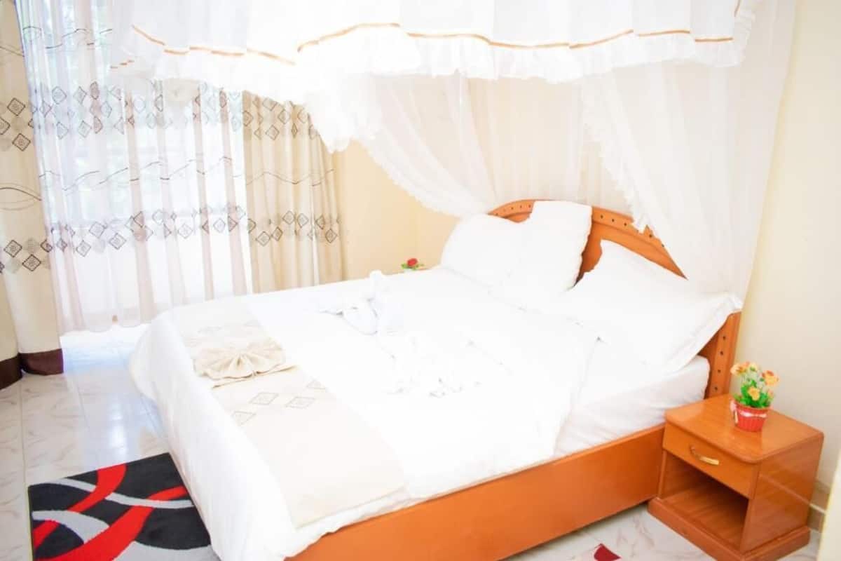 Una cama bien hecha con sábanas blancas, cabecera de madera y mesita de noche con un jarrón de flores.