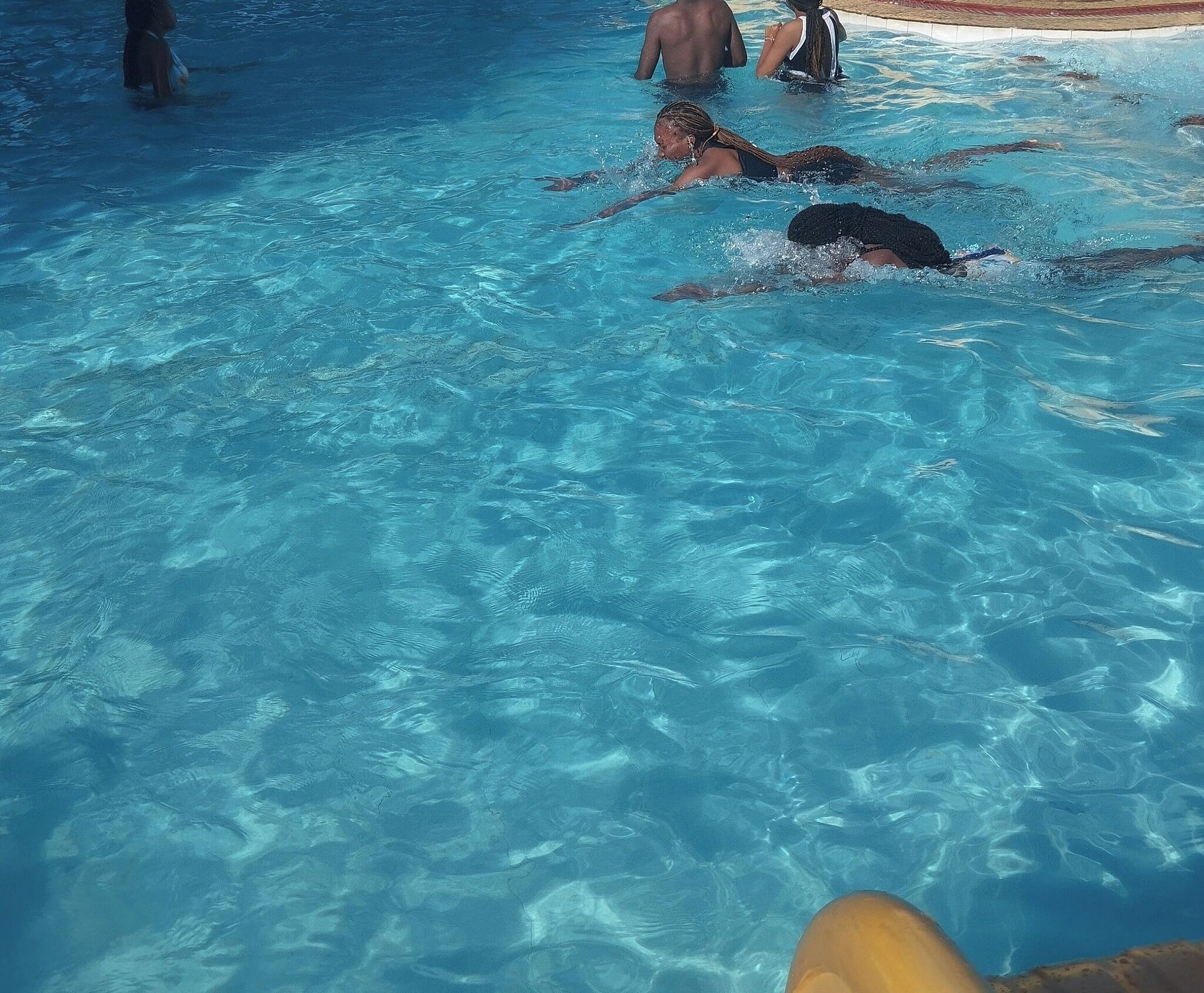A swimming pool with clear blue water, swimmers, and a poolside area.