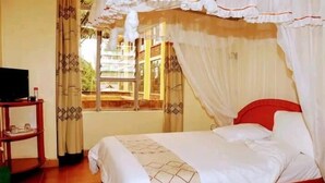 Un dormitorio con una cama, un televisor sobre un mueble bajo y una ventana con cortinas.
