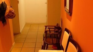 Ein Flur mit einer Sitzecke, ausgestattet mit Stühlen und einer Bank, einer Tür am Ende und einem Kleiderständer links.
