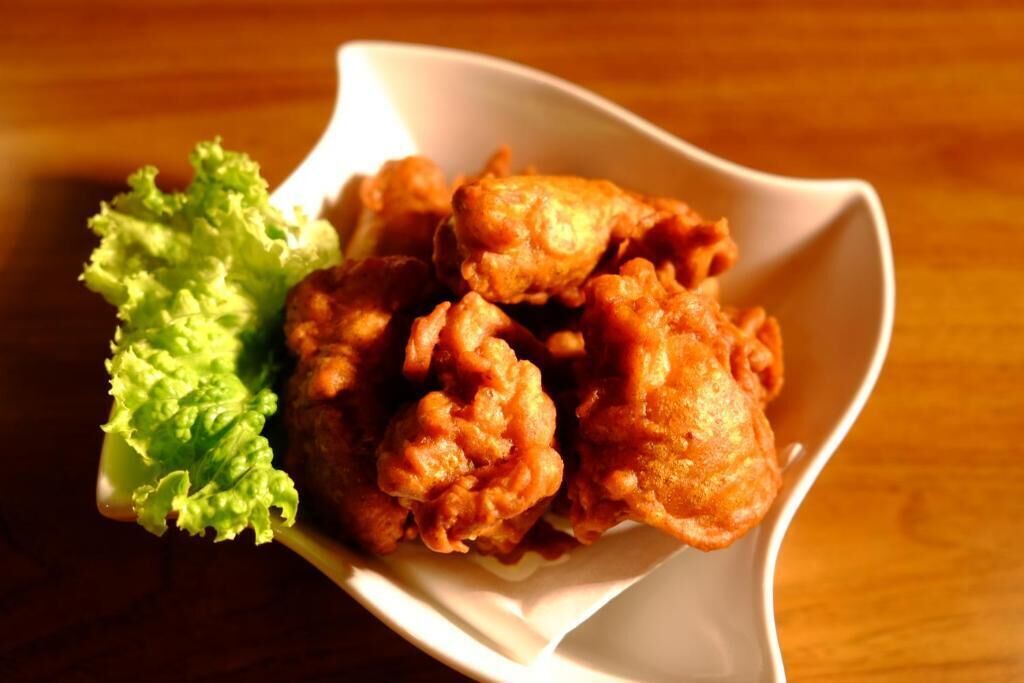 A white bowl containing fried chicken pieces and a leaf of lettuce on a wooden table.
