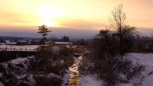 Schneebedeckte Landschaft mit einem Bach und einer Brücke im Hintergrund.