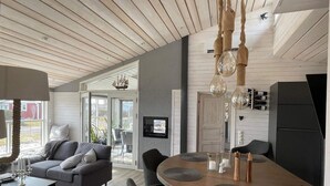 A modern living room with a grey sofa, a wooden dining table with chairs, and a kitchen area with a black refrigerator and wine bottles. - 5 Star Holiday Home in Skummeslovsstrand (Skummesloevsstrand)