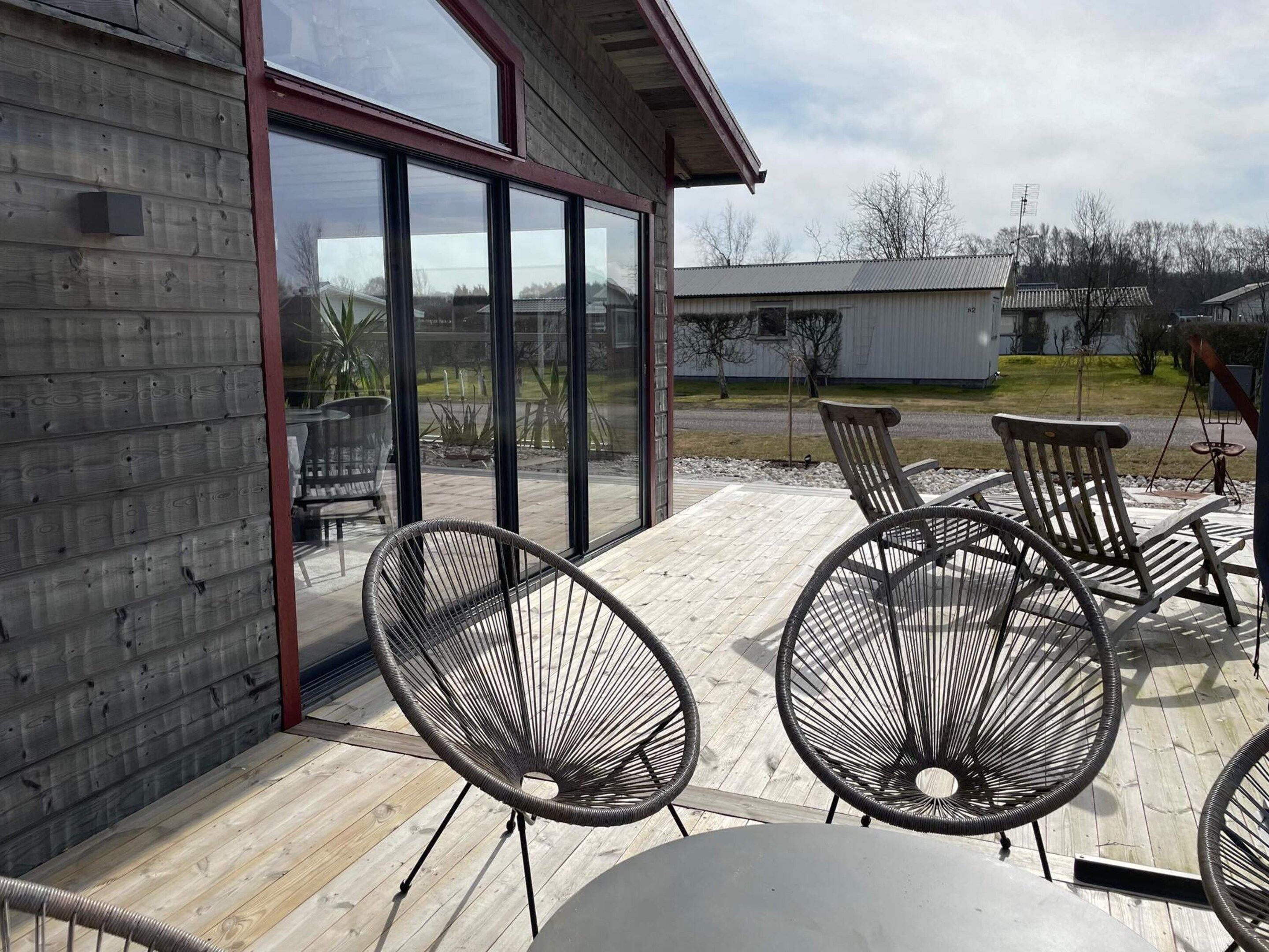 Eine Terrasse mit Gartenmöbeln, darunter Stühle und ein Tisch, und ein Gebäude mit großen Fenstern.