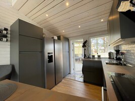 A modern kitchen with a built-in stainless steel refrigerator, a wooden dining table, and a view of the outdoors through a large window.