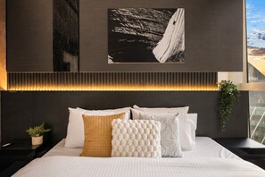 A modern bedroom with a bed, pillows, a headboard with built-in lighting, and a cityscape view. - The Skyline Grand | Panoramic Views + Free Parking! (Melbourne)