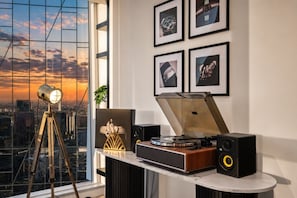 A modern interior with a city view, a turntable, speakers, and framed pictures on the wall. - The Skyline Grand | Panoramic Views + Free Parking! (Melbourne)