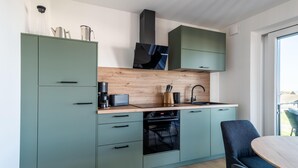 A modern kitchen with light green cabinets, a wooden countertop, a built-in oven, and a dining area with a round table and chairs. - The View B10 AHOI - Sea view, balcony, 2nd floor, shared. (Dagebüll)