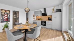 A modern kitchen with a dining area, featuring a round wooden table, grey upholstered chairs, and a pendant light. - The View G01 Licht-Luft-Ebbe und Flut - Balcony, Barbecue, Parking Space (Dagebüll)