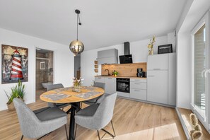 Eine moderne Küche mit Essbereich, ausgestattet mit einem runden Holztisch, grau gepolsterten Stühlen und einer Pendelleuchte.
