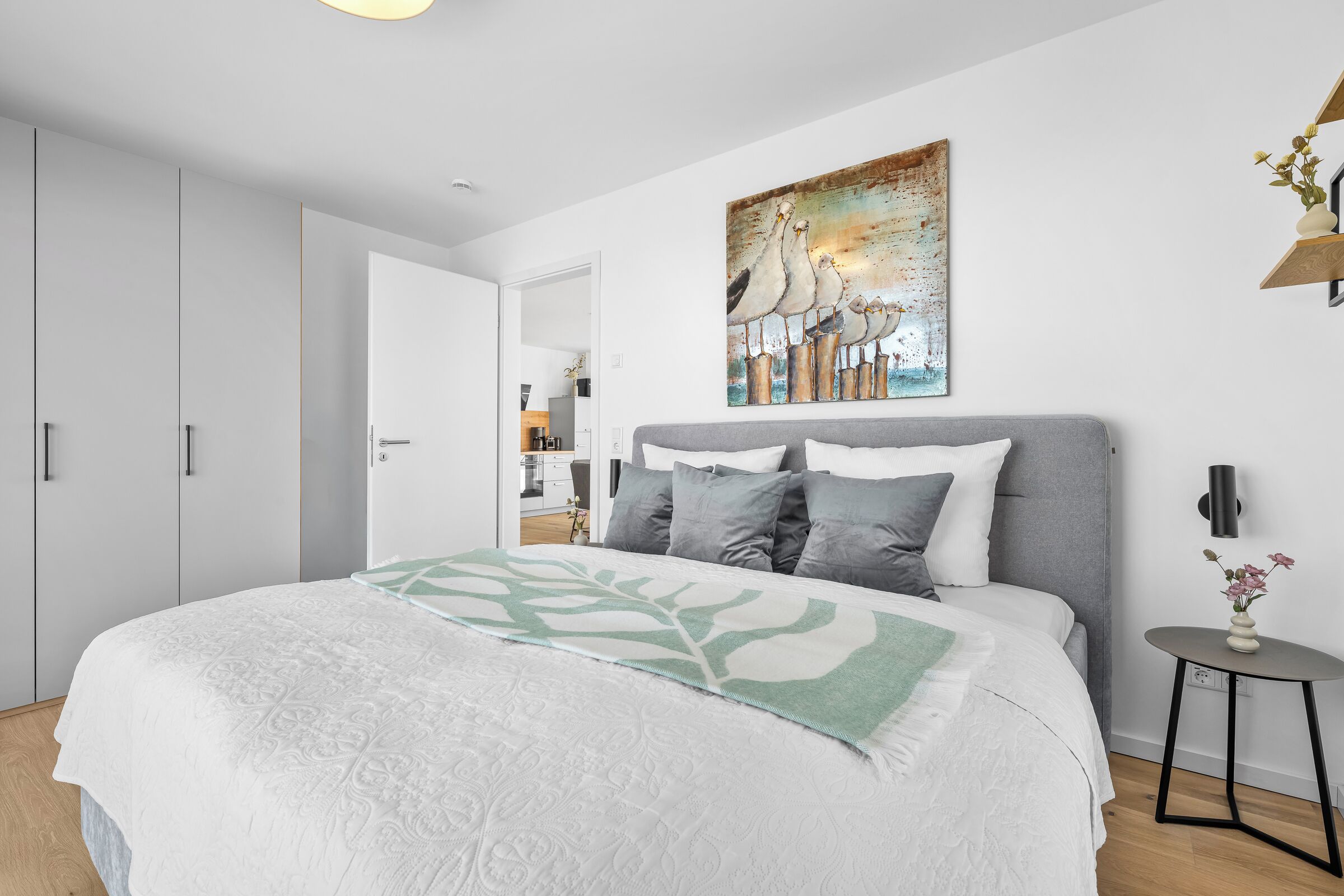 A modern bedroom with a large bed, a grey headboard, and a painting above it.
