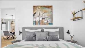 A modern bedroom with a large bed, grey pillows, a wall-mounted artwork of birds, and a bedside table with a vase. - The View G01 Licht-Luft-Ebbe und Flut - Balcony, Barbecue, Parking Space (Dagebüll)