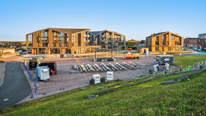 A modern building with multiple floors, outdoor seating, and flags. - The View G01 Licht-Luft-Ebbe und Flut - Balcony, Barbecue, Parking Space (Dagebüll)