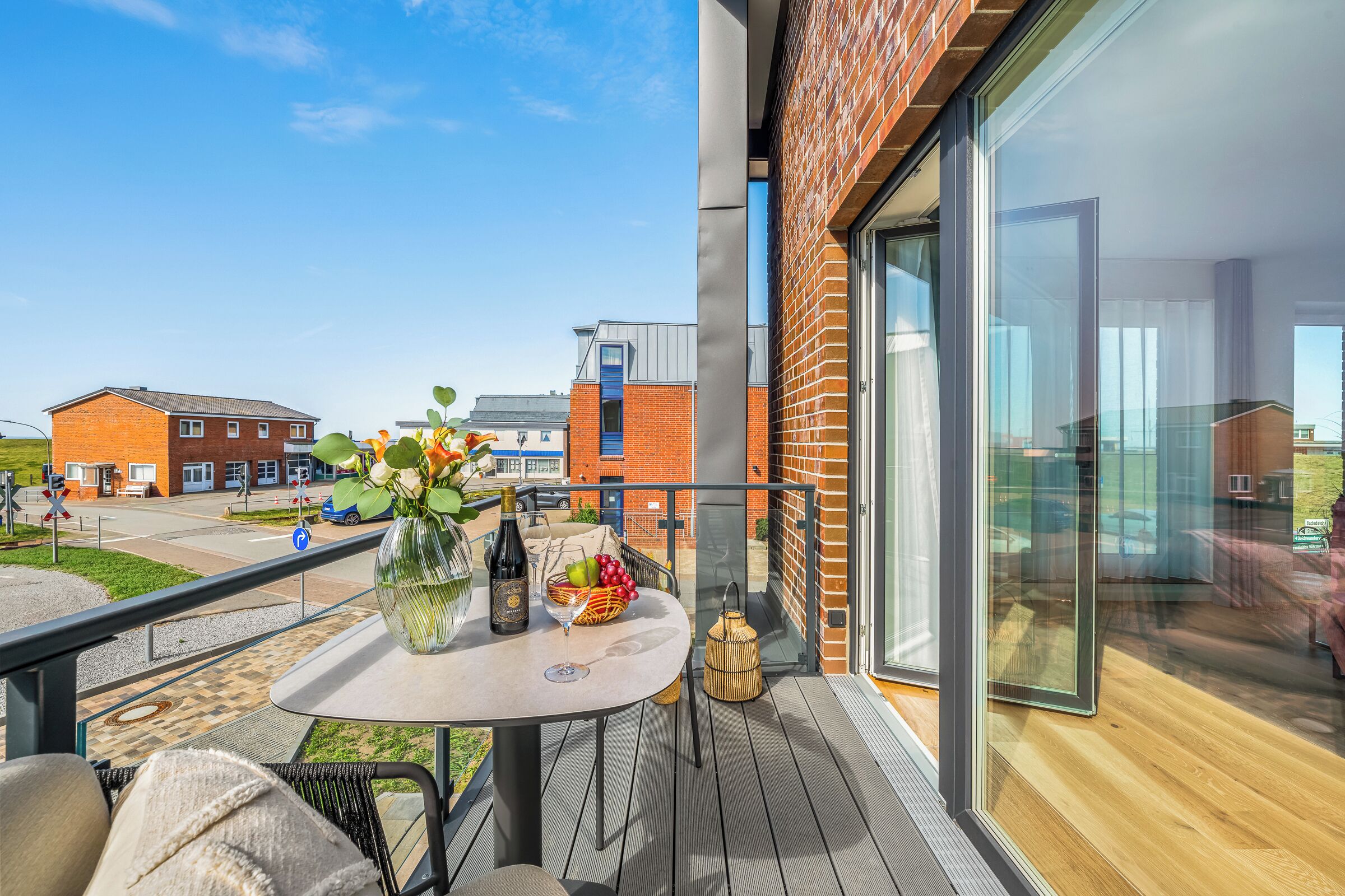 A balcony with a table set for two, a bottle of wine, and a vase of flowers.
