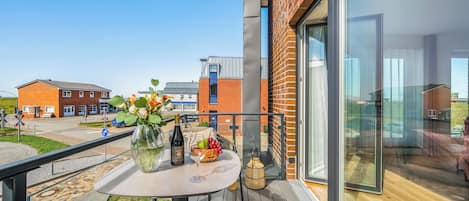 A balcony with a table set for two, a bottle of wine, and a vase of flowers.