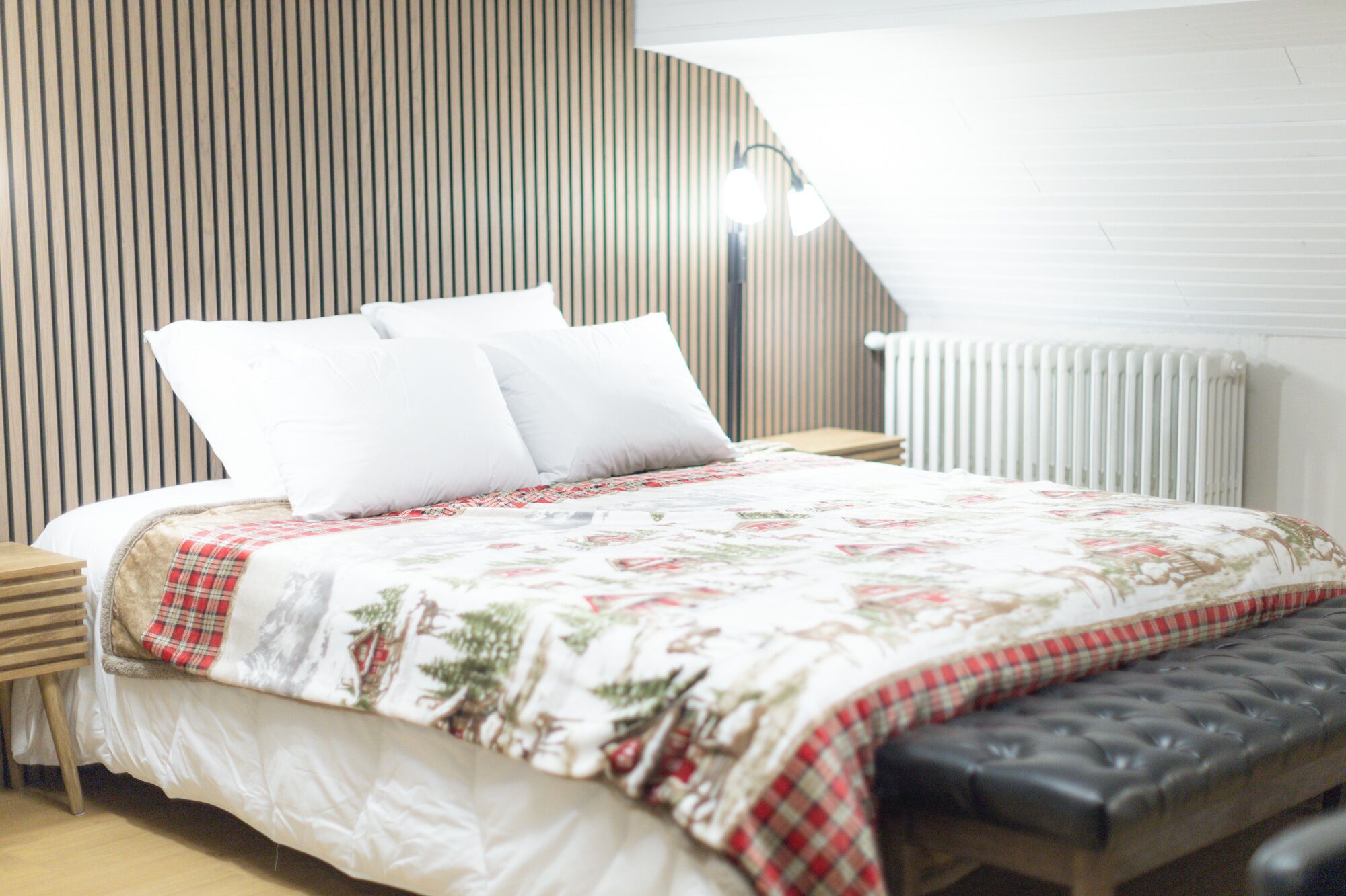 Een keurig opgemaakt bed met een bloemenbedekker, een geruit plaid en een zwart beklede bank.