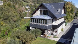 Ein zweigeschossiges Haus mit geneigtem Dach, einem Balkon mit Glasgeländern und einem Steinfundament.