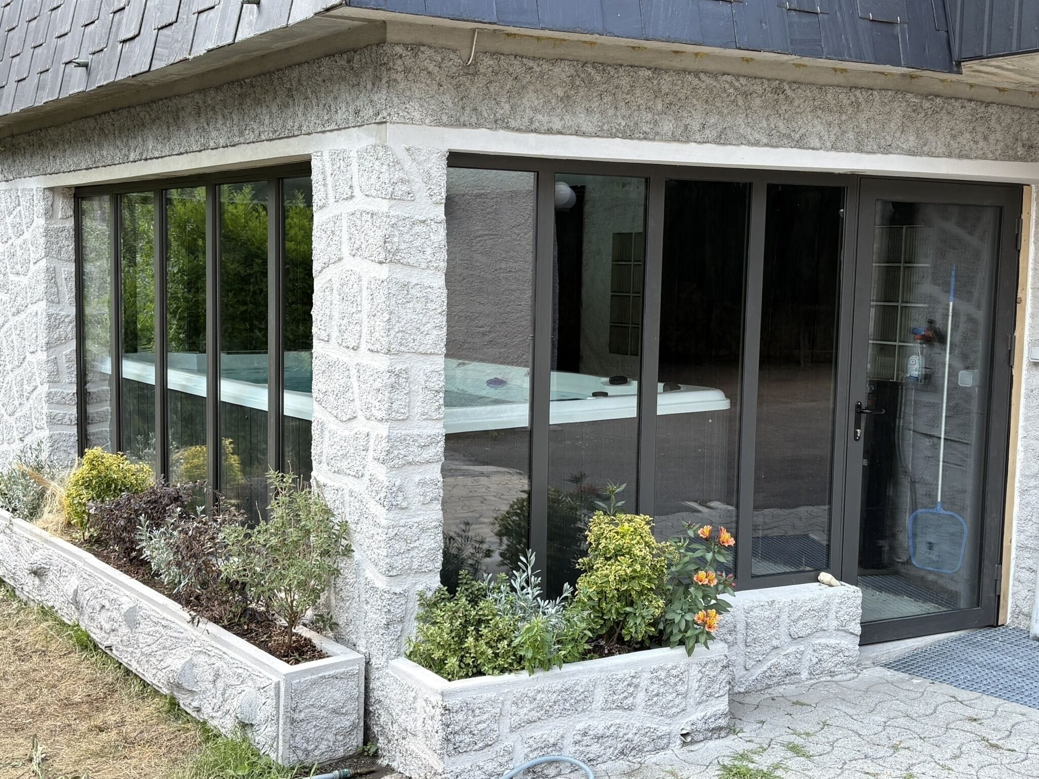 Ein modernes Haus mit einer glasvergrößerten Terrasse, Steinwänden und einem sichtbaren Whirlpool.