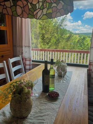 A wooden table with a lace tablecloth, two wine bottles, a bowl of berries, and a vase with flowers on a balcony overlooking a green landscape. - Forest house in the Ore Mountains (Augustusburg)