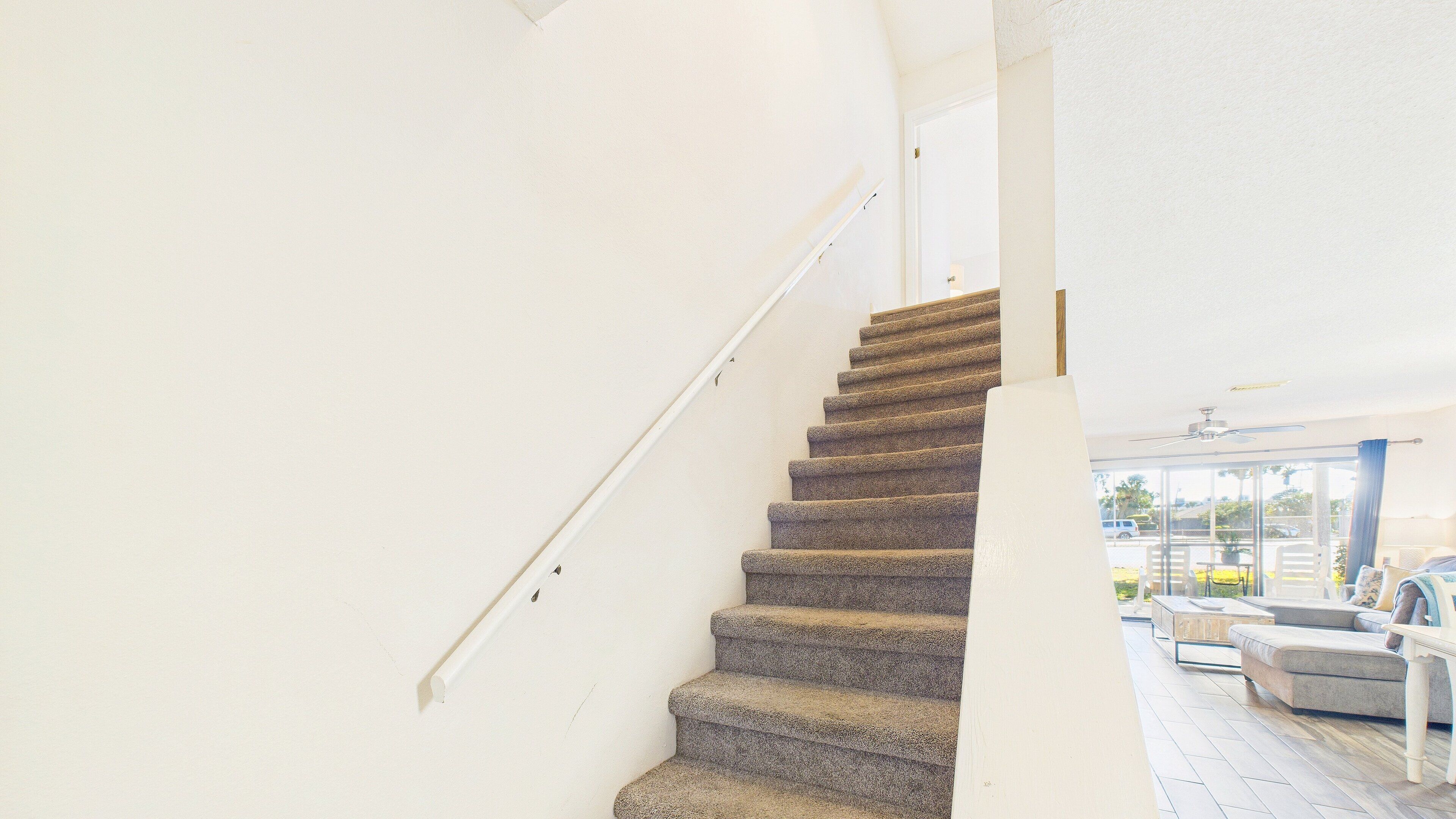 A staircase with carpeted steps leading to a balcony area with outdoor furniture.
