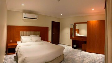 Habitación de hotel con una cama grande, cabecera de madera, armario empotrado, un espejo y un equipo de aire acondicionado.