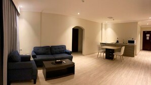 A modern living room with a sofa, a coffee table, and a dining area with a desk and chairs. - Amaken For Residential Units (Al-Hofuf)