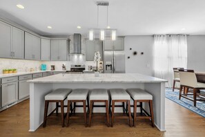 Una cocina moderna con armarios grises, una isla grande con taburetes altos, electrodomésticos de acero inoxidable y una lámpara colgante.