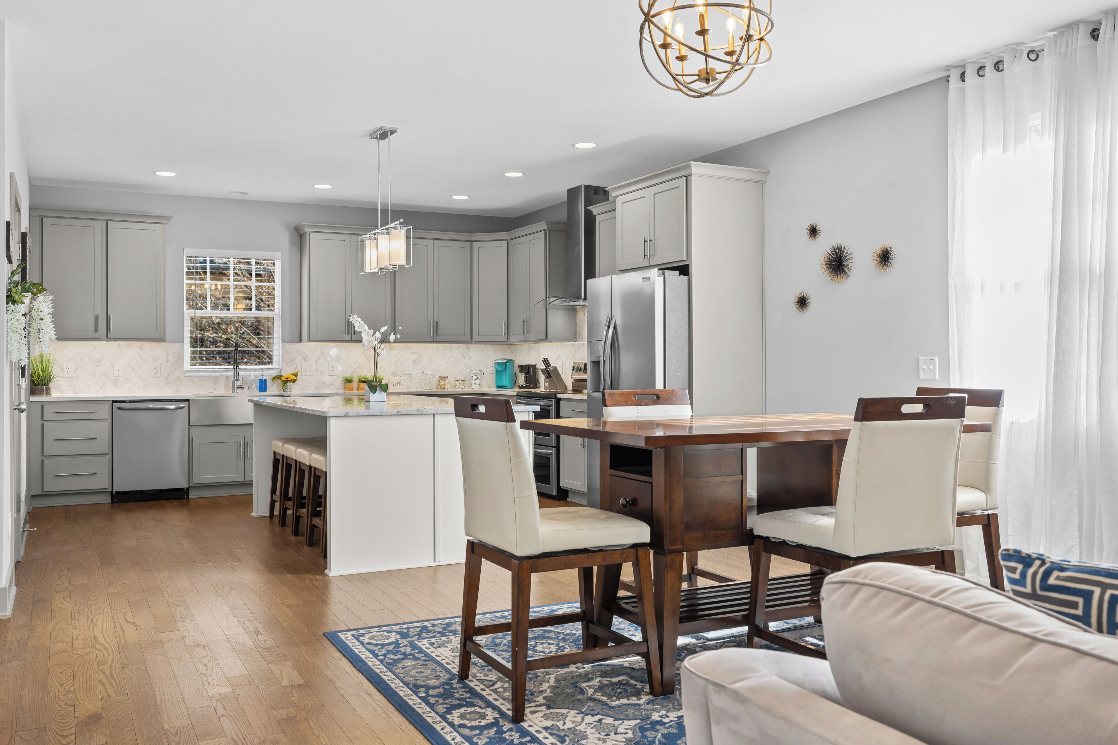 A modern kitchen with grey cabinets, a central island, and a dining area with wooden chairs.