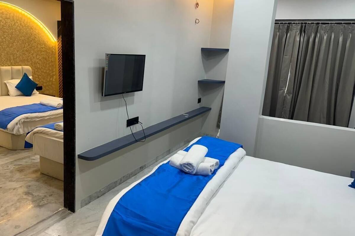 Ein Hotelzimmer mit zwei Betten, einem an der Wand befestigten Fernseher, einer eingebauten Ablage und einem Fenster mit Vorhängen.