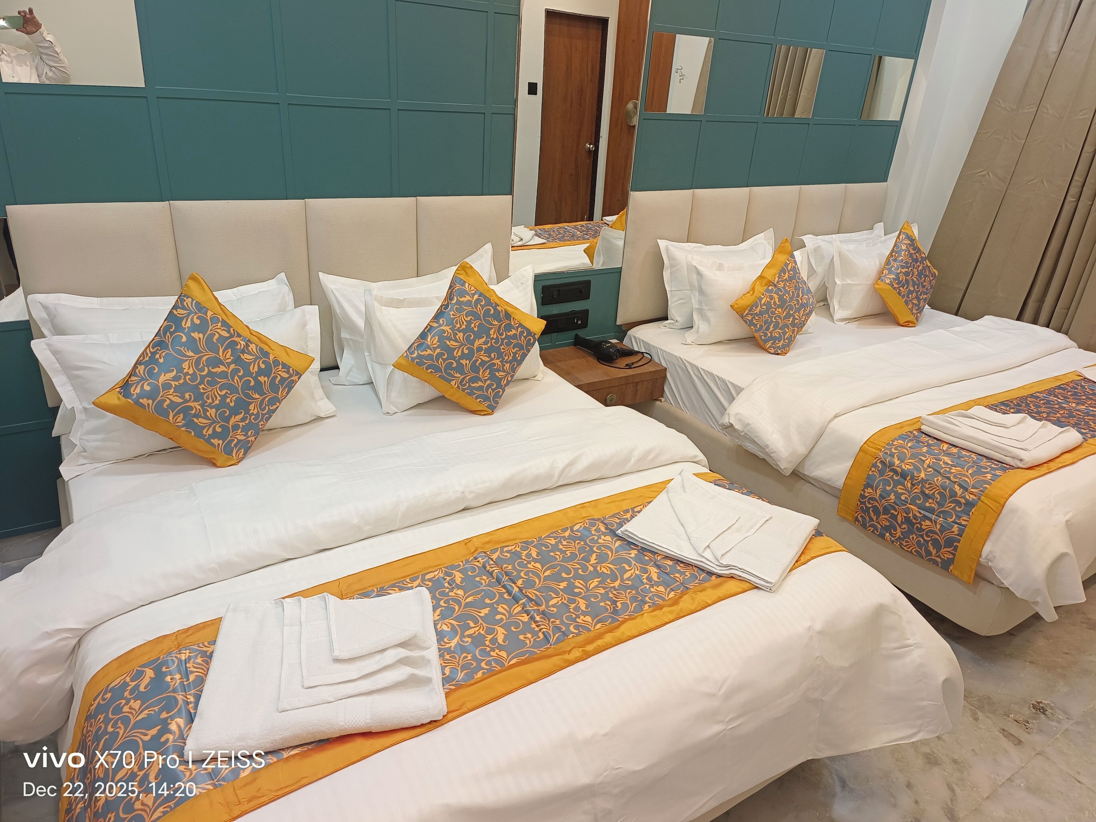 Une chambre d’hôtel avec deux lits, chacun agrémenté de draps blancs et d’oreillers décoratifs. Une table de chevet en bois se trouve entre les lits, et un miroir est accroché au mur.