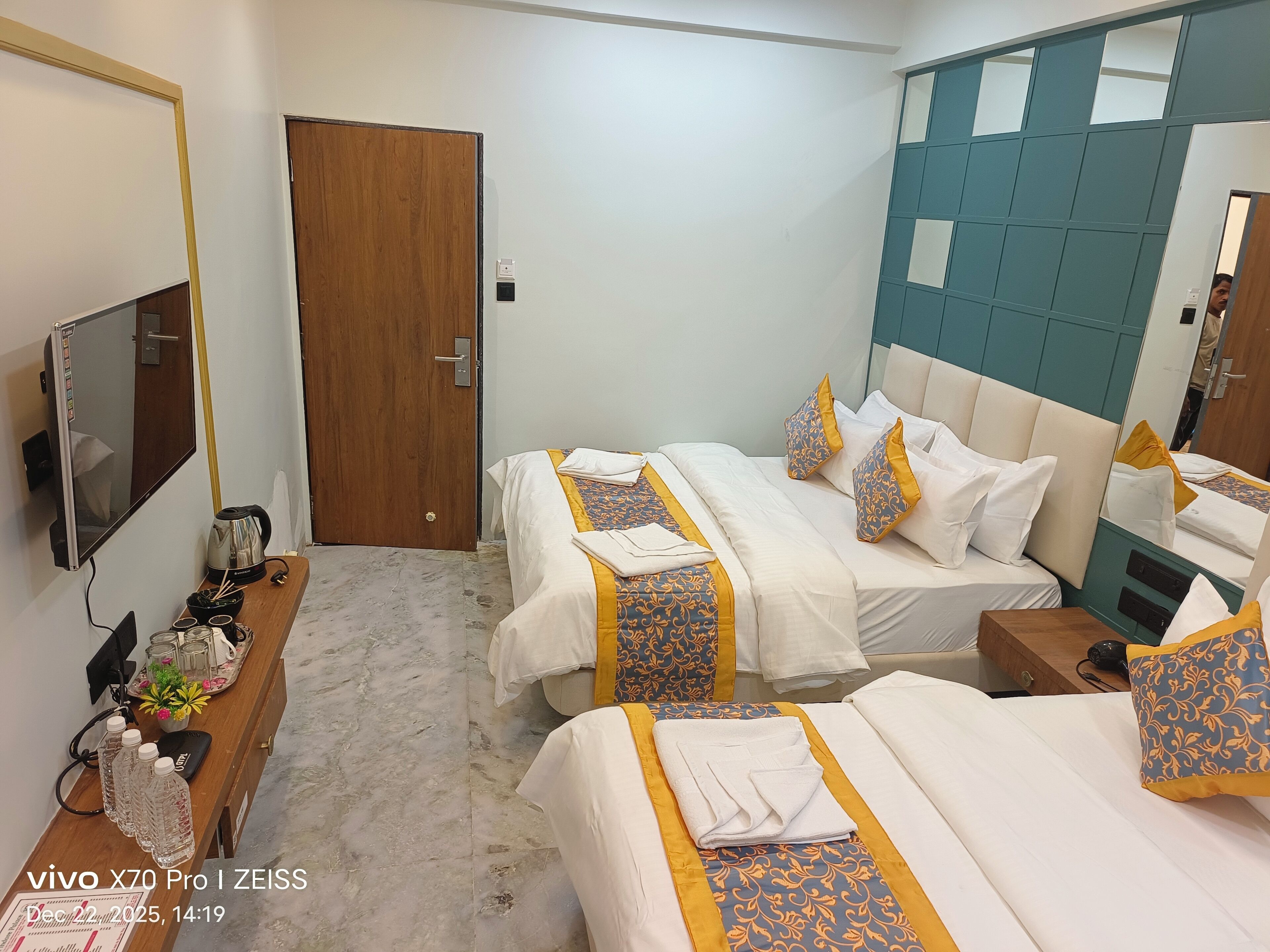 Habitación de hotel con dos camas, un escritorio de madera con hervidor, televisor y espejo.