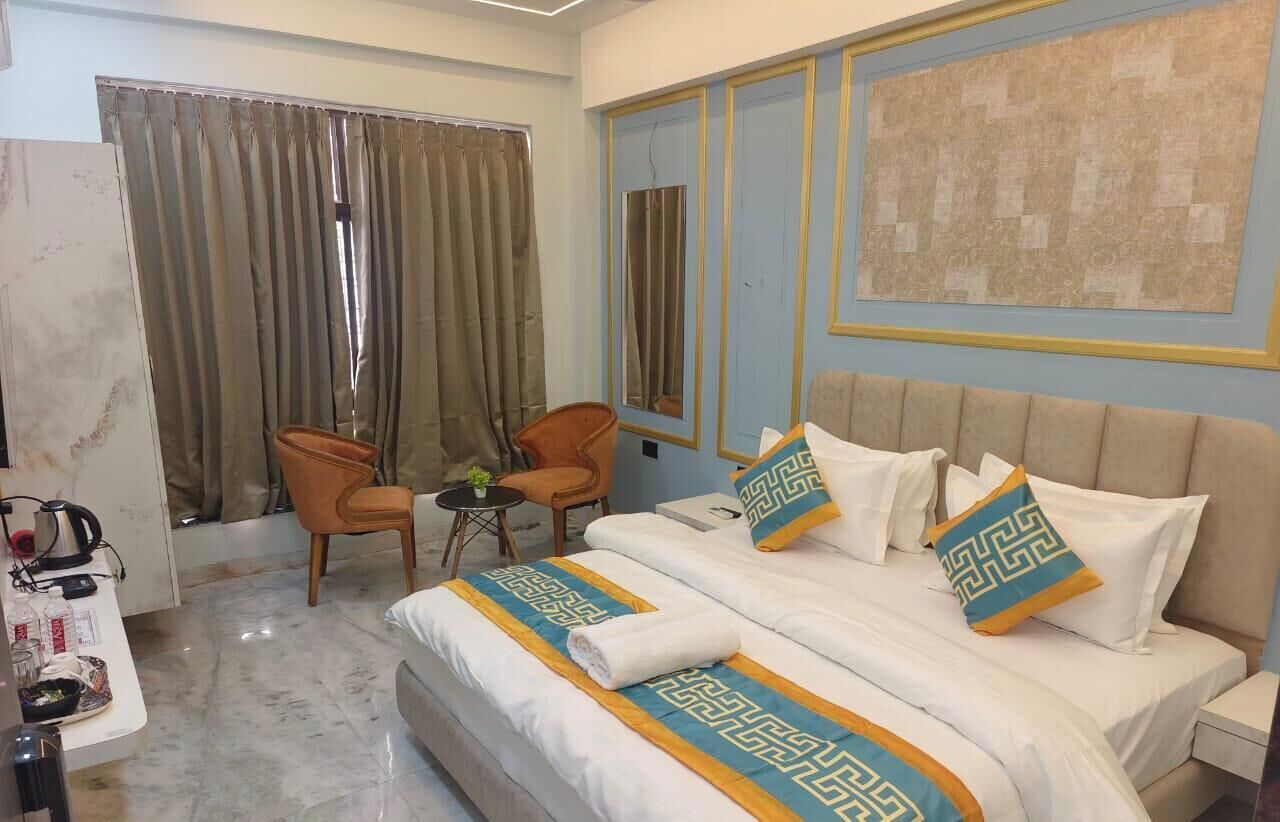 A hotel room with a bed, two chairs, a small table, and a large window with curtains.