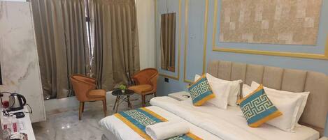 A hotel room with a bed, two chairs, a small table, and a large window with curtains.
